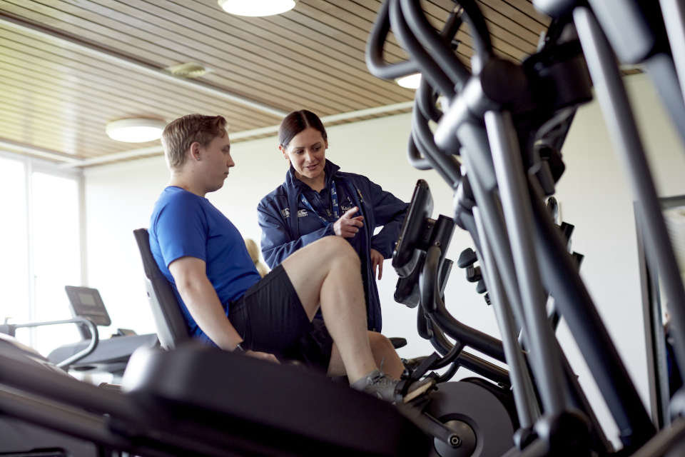 A rehabilitation and exercise science professional instructing a patient about a piece of gym equipment at the fitness centre at Keele University.