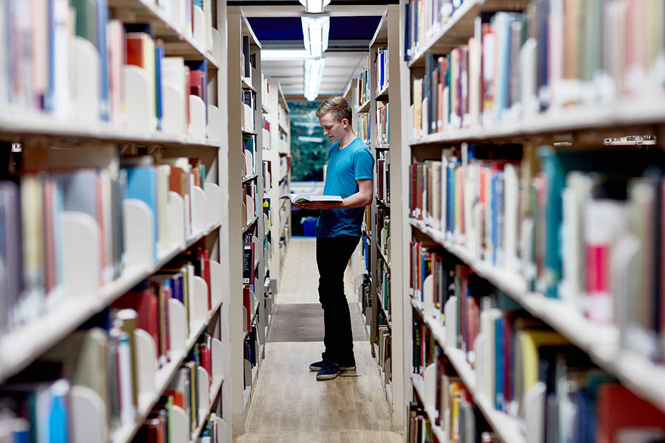 Student standing looking at books in library