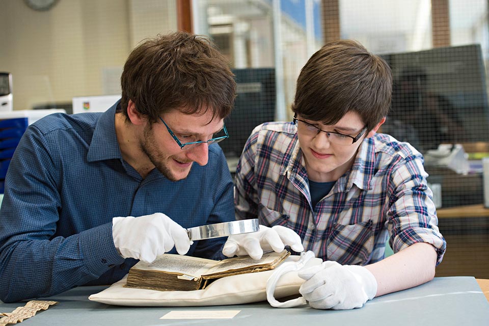 Student and lecturer using magnifying glass with book
