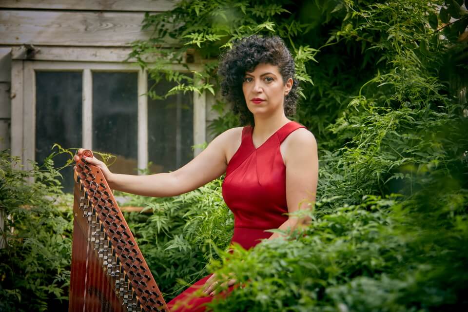 photograph of Maya sitting in a garden wearing a red dress and holing the quanun