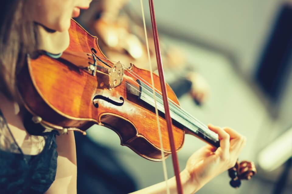 Image of someone holding a violin and using a bow all you can see is the performers hands