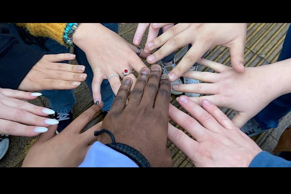 hands with a range of different skin tones reaching in to the centre of the image