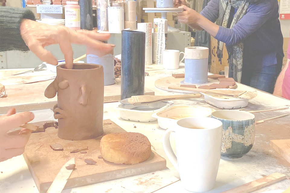 A ceramics workshop - tools and clay are on the table and someone has made a pot with a face