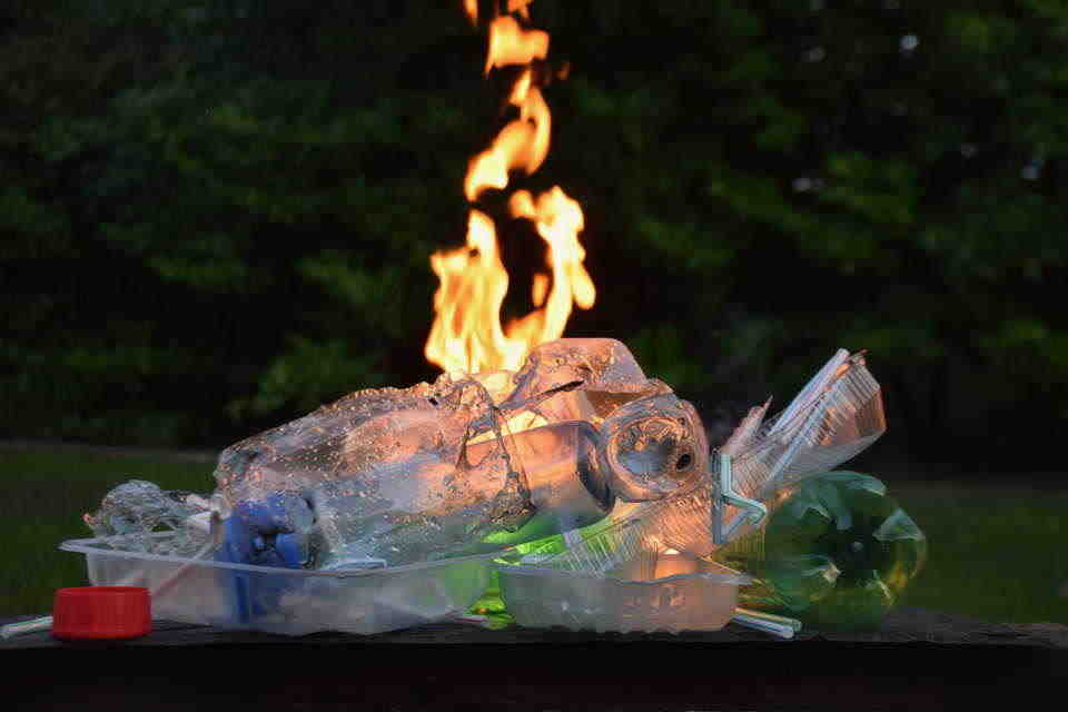 image of a pile of plastic waste with a fire burning behind it