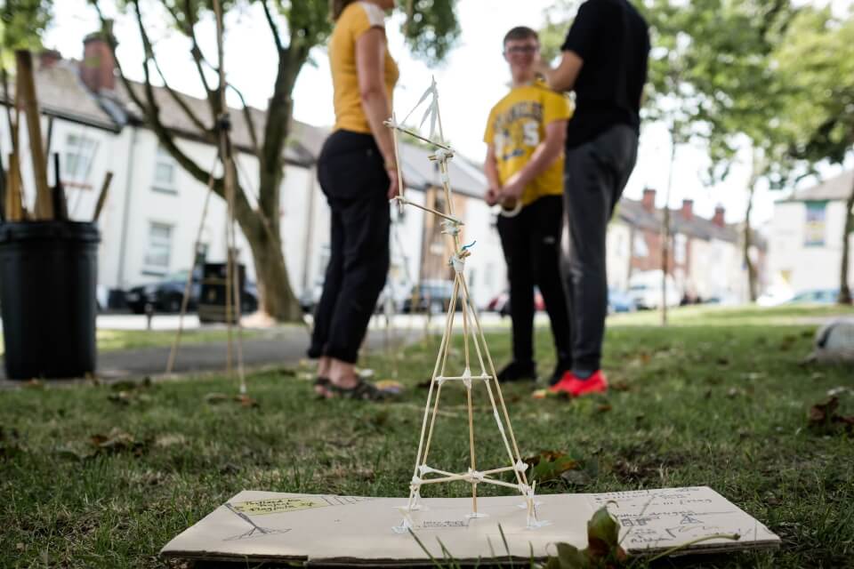 image of people standing above a mini bamboo model they have made on the grass