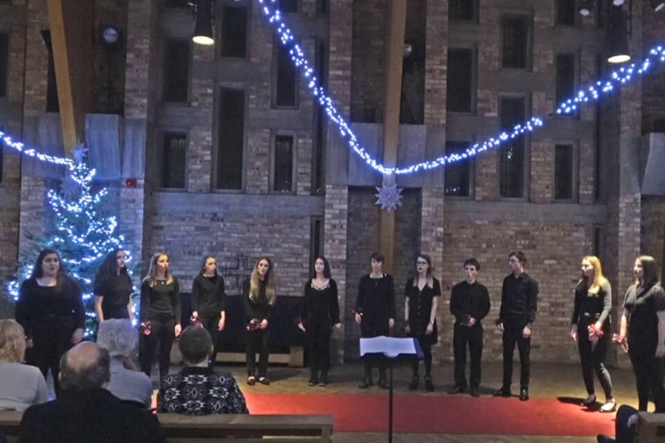 Group of singers wearing black inside the Chapel with fairy lights above them