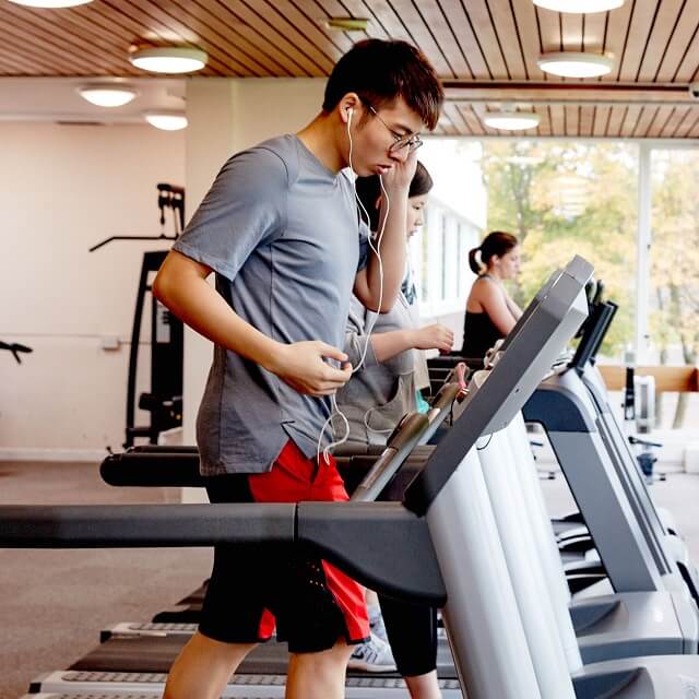 Student using treadmill at the gym listening to music through headphones.